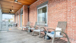 Un bâtiment en briques doté d’une terrasse en bois, de fauteuils à bascule et d’une table avec des chaises.