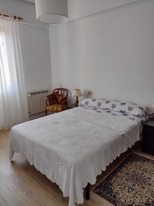 A bedroom with a bed, a chair, a lamp, a radiator, and a rug.