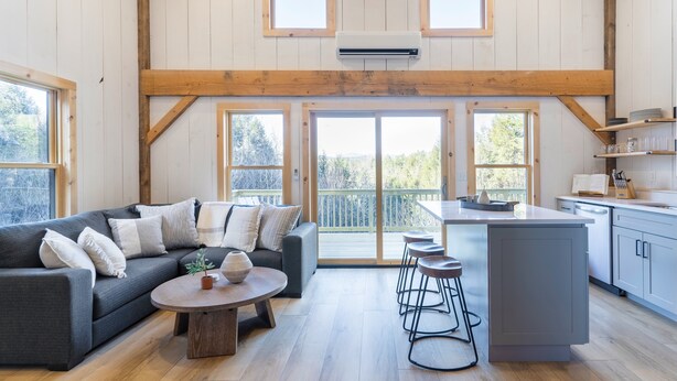 A spacious living area with a gray sofa, a coffee table, and a kitchen area with a bar counter and stools.