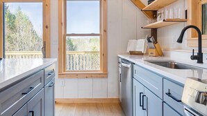 A modern kitchen with wooden beams, a large window, and a view of trees.