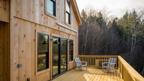 A wooden cabin with a deck, large windows, and a view of the surrounding forest.