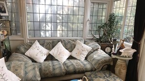 Ein gemütliches Wohnzimmer mit einer gemusterten Couch, dekorativen Kissen, einem Beistelltisch mit einer Uhr und einem Topf mit einer Pflanze.