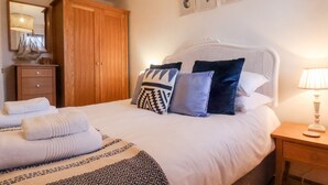 A neatly made bed with patterned blankets and pillows, a wooden wardrobe, a bedside table with a lamp, and a wall-mounted mirror. - Stoker's Rest (Whitby)