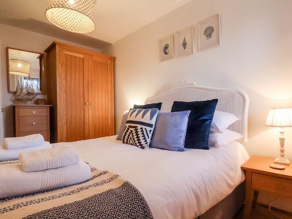 Ein ordentlich bezogenes Bett mit gemusterten Decken und Kissen, ein Holzschrank, ein Nachttisch mit Lampe und ein an der Wand befestigter Spiegel.