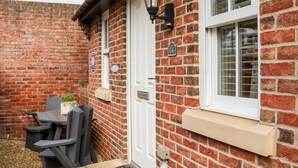 A brick house with a white door, a window with a white frame, and a small porch area with a bench and a potted plant. - Stoker's Rest (Whitby)