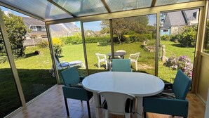 Un patio cubierto con una mesa redonda y sillas, vista a un jardín, y una casa al fondo.