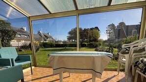 Un invernadero con una mesa y sillas, un tapete estampado y vistas a un jardín y casas.
