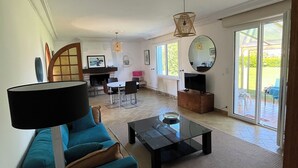 Una sala de estar con un sofá, una mesa de centro y un televisor. Hay una zona de comedor con sillas y una mesa.