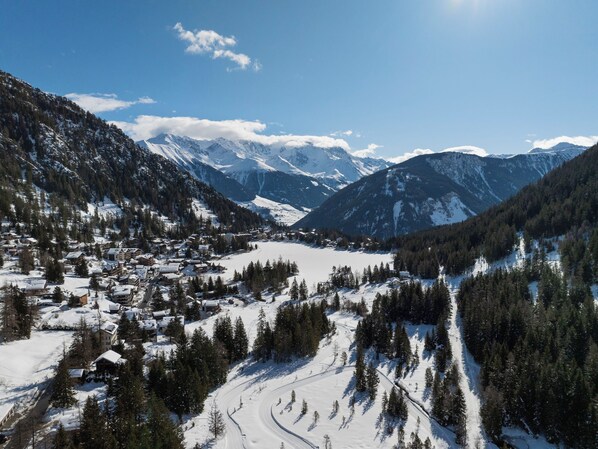Een besneeuwd bergstadje met gebouwen en een skipiste.