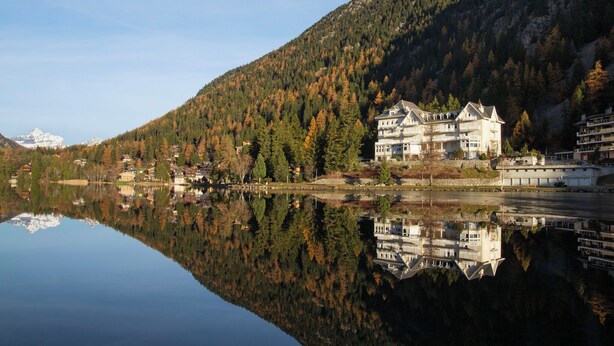 Ein großes, mehrstöckiges Hotel mit Spiegelbild im See, umgeben von bewaldeten Bergen.