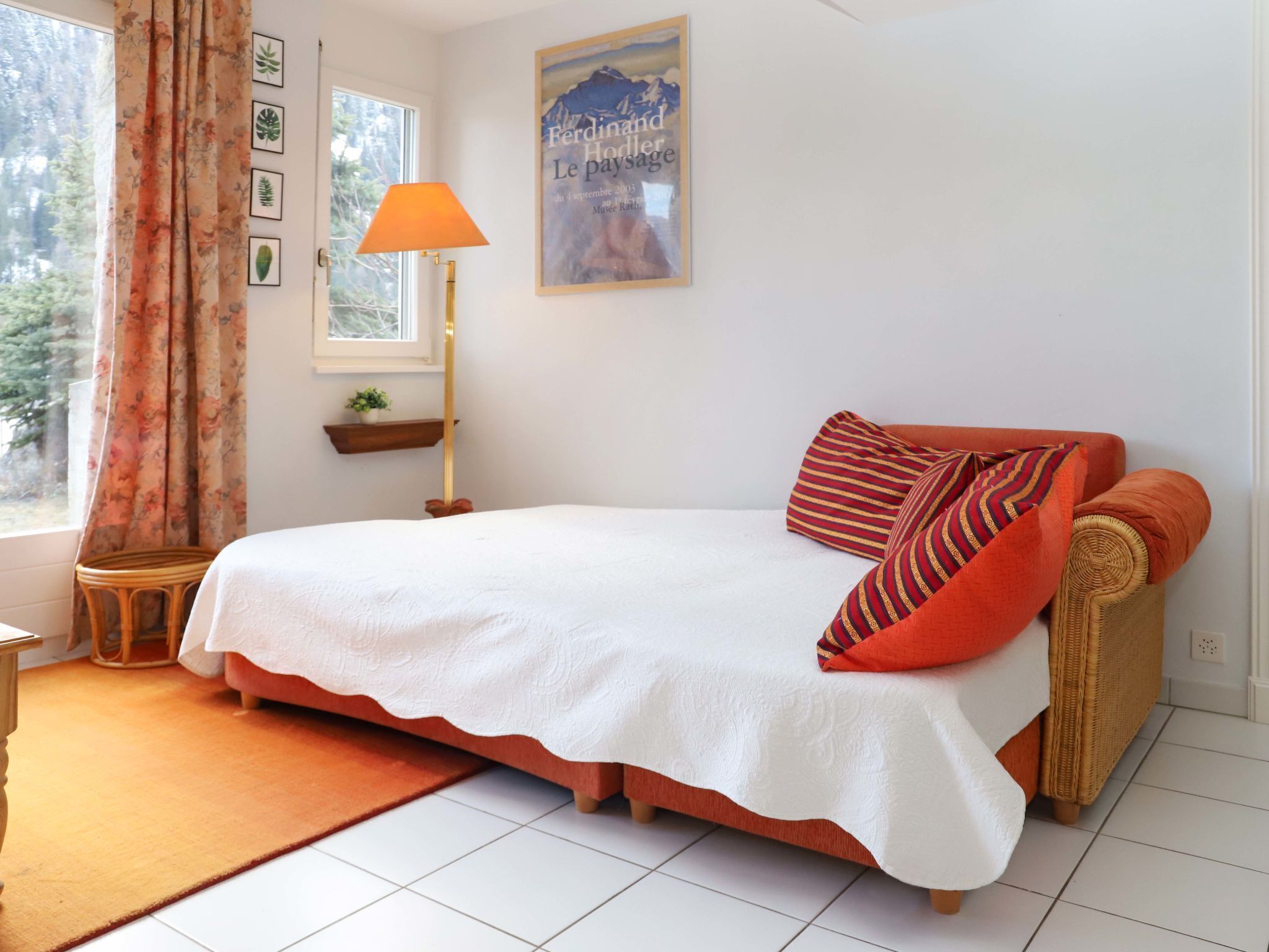 Ein Schlafzimmer mit einem Bett, einem Nachttisch, einer Lampe, einem Fenster mit Vorhängen, einem an der Wand befestigten Regal mit einer Pflanze und einem gerahmten Bild.