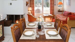 Ein Esszimmer mit Holztisch, gedeckt für sechs Personen, umgeben von Stühlen, einem Kamin und Blick ins Freie.