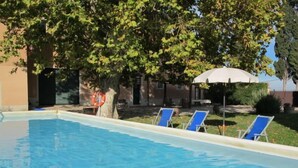 Une piscine à l’eau d’un bleu cristallin, entourée de chaises longues et d’un arbre.