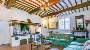 Un intérieur rustique avec des poutres apparentes, une cuisine équipée d’un poêle et un canapé vert.