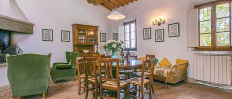 Un comedor con una mesa y sillas de madera, un sillón verde, un armario y un radiador.