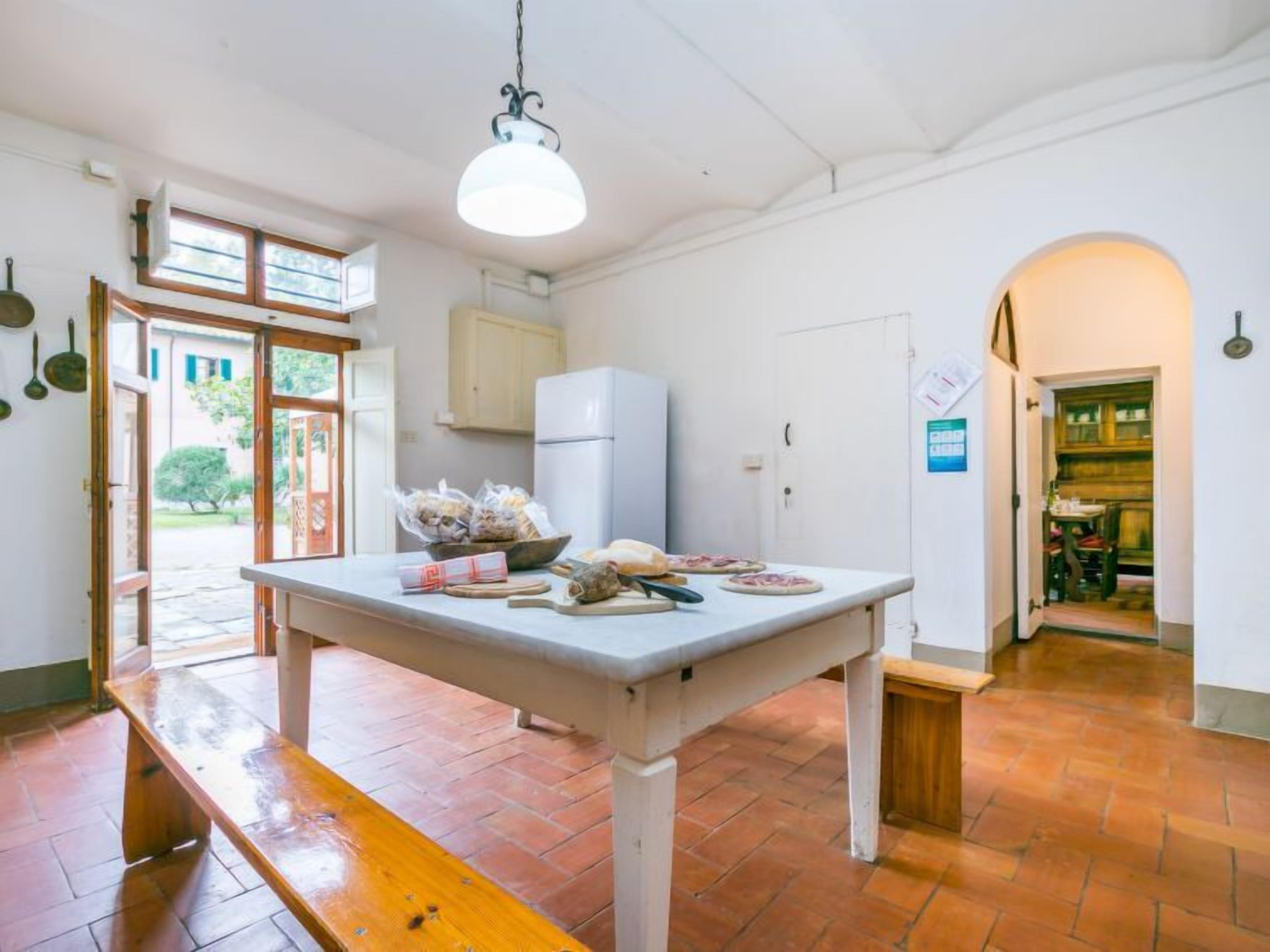 A kitchen with a white table, a hanging light fixture, a refrigerator, and a wooden bench.