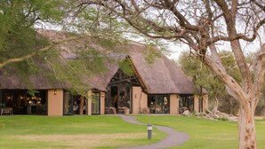 A thatched-roof building with outdoor seating and a paved pathway leading to it. - Okapuka Safari Lodge (Windhoek)