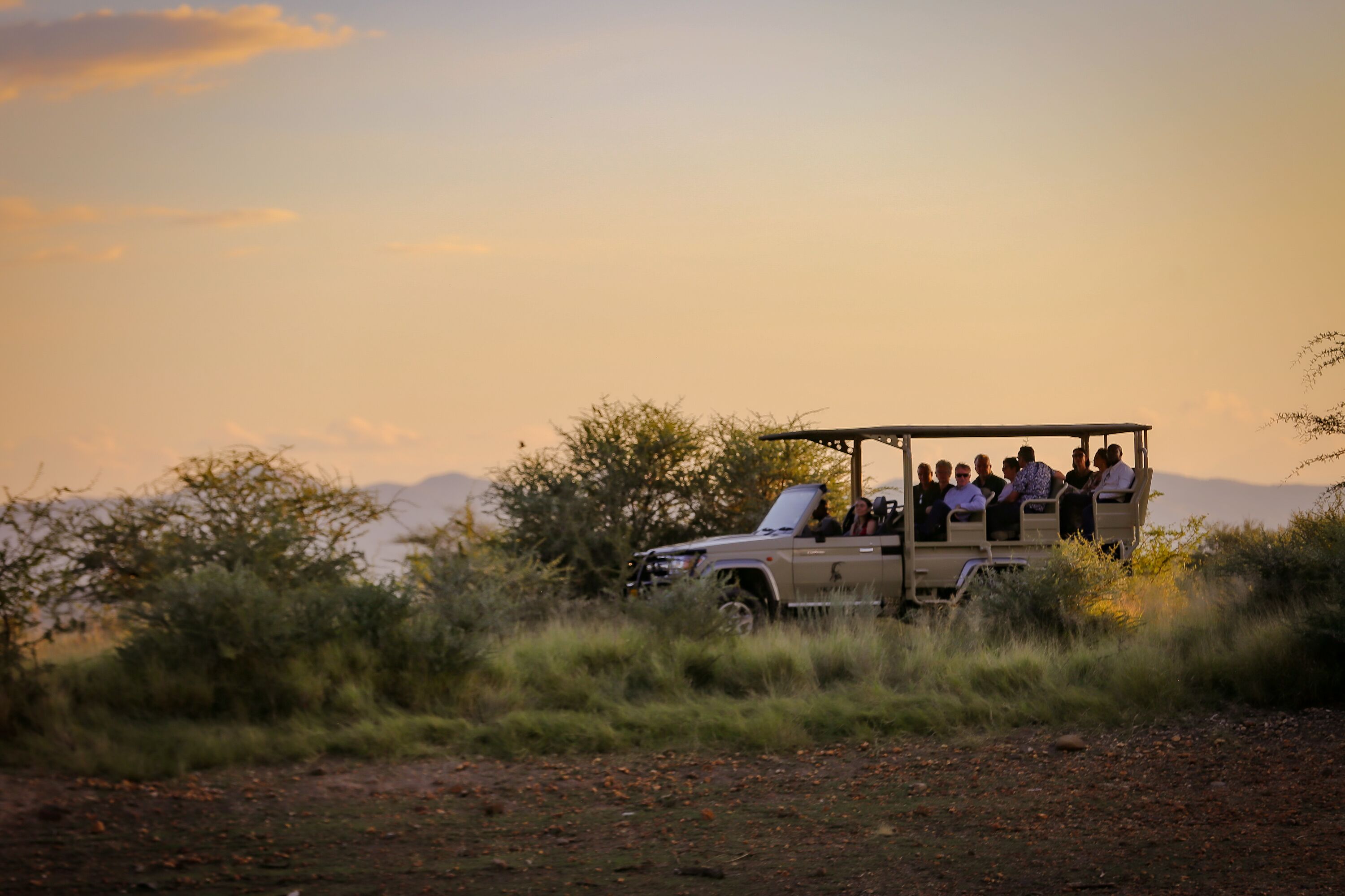 A safari vehicle with passengers, surrounded by natural landscape and mountains in the background.
