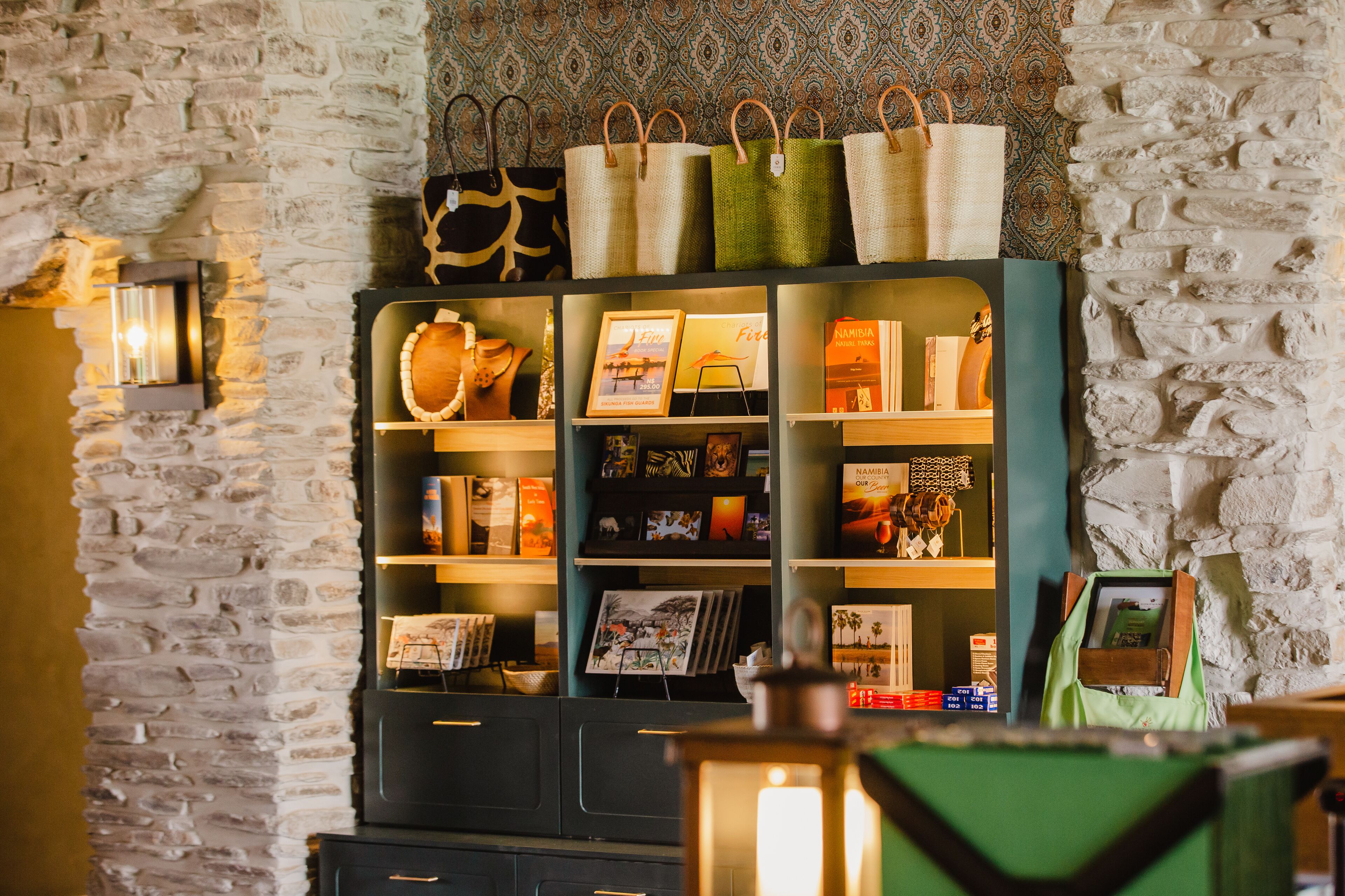 Een kamer met een stenen muur, een boekenplank met diverse spullen, en een groene tas op een tafel.