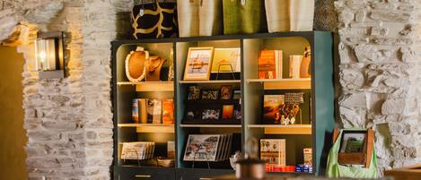 Een kamer met een stenen muur, een boekenplank met diverse spullen, en een groene tas op een tafel.