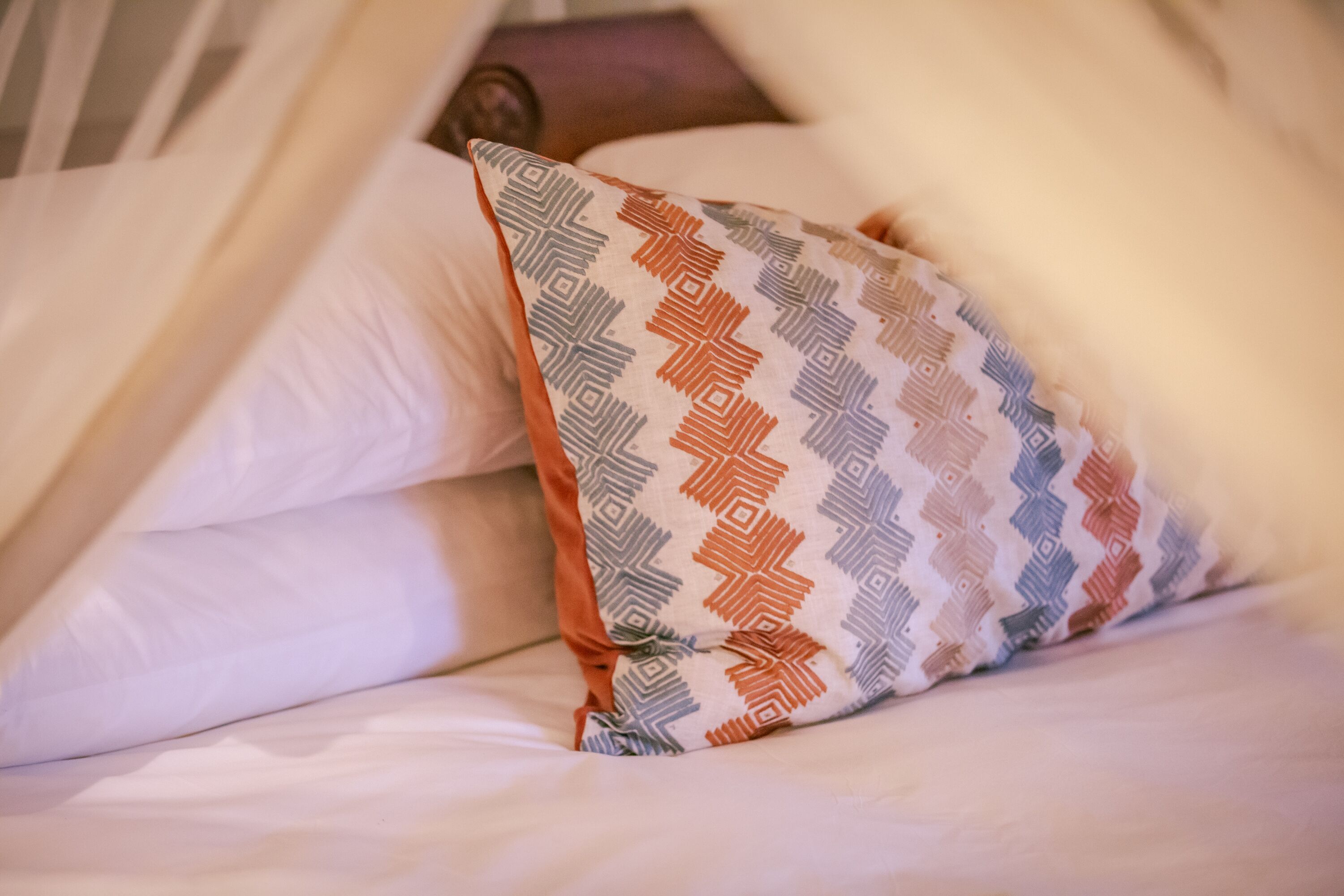 A bed with white bedding and a patterned pillow.