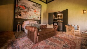 A cozy room with a large bed, a brown leather sofa, a wicker chair, and a painting on the wall. - Okapuka Safari Lodge (Windhoek)