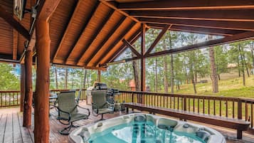 A wooden deck with a hot tub, chairs, and a grill.