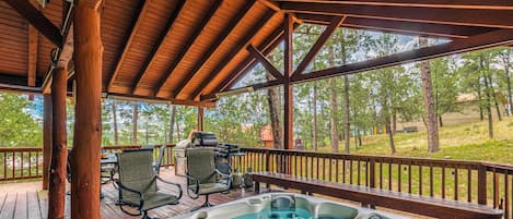 A wooden deck with a hot tub, chairs, and a grill.