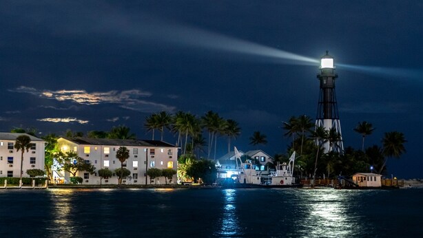 A coastal scene with a prominent lighthouse, a marina with boats, and buildings along the shore. - Ocean Mist: Chef's Kitchen & Private Pool (Pompano Beach)