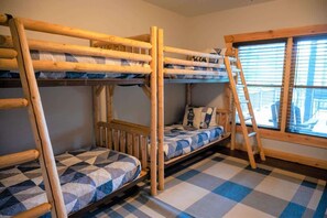 Een slaapkamer met stapelbed, een geruite vloer, een raam met zonwering en een houten trap.