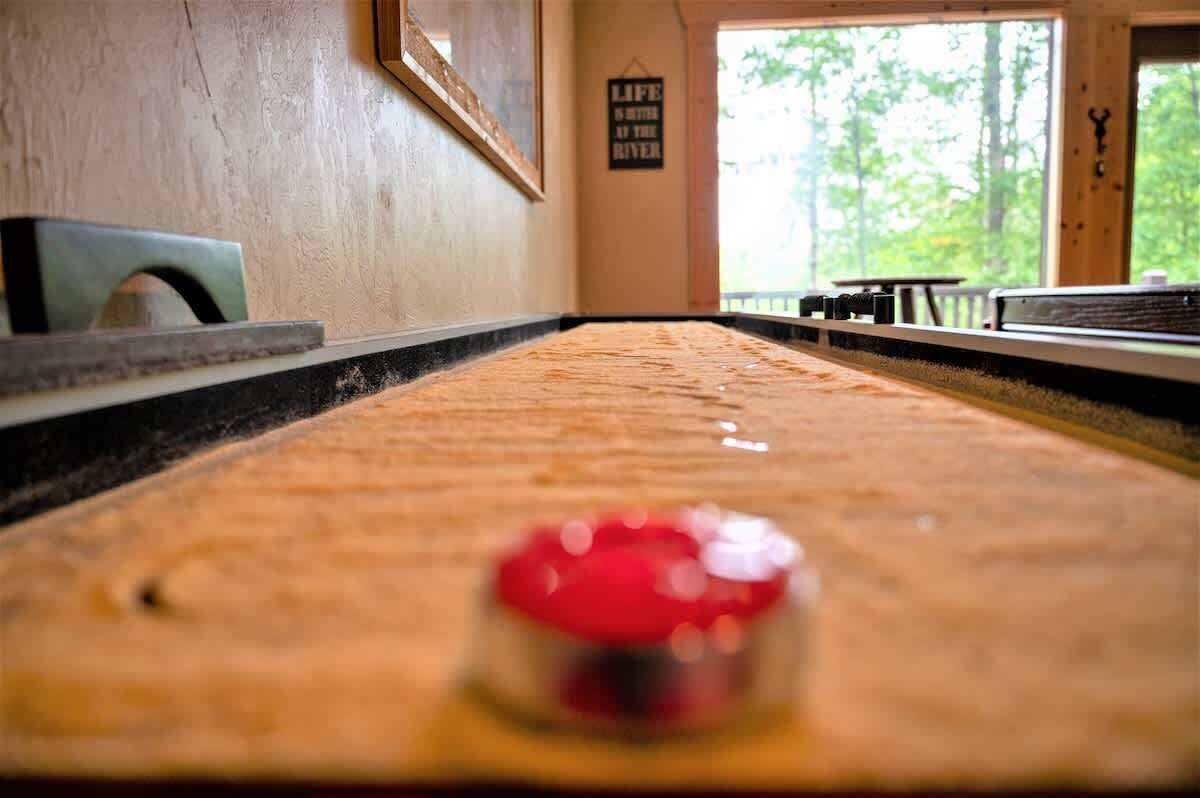 A wooden table with a red object in the foreground, a framed picture on the wall, and a sign that reads 'LIFE IS BETTER AT THE RIVER'.