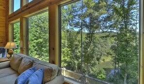 A room with a large window overlooking a forested area and a body of water.