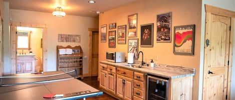 A room with a ping pong table, wooden cabinets, a microwave, and a door with a handle.