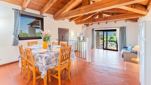 A dining area with a wooden ceiling, a table set for four, and a view of the outdoors through a window. - Graziose Ville con A.C e piscina comune (Stintino)