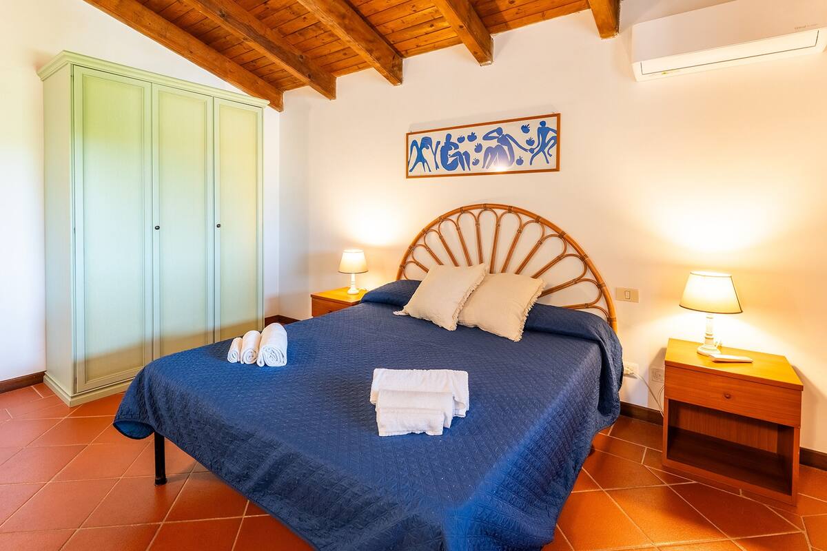 A bedroom with a bed, two bedside tables with lamps, a wardrobe, and a wall art piece.