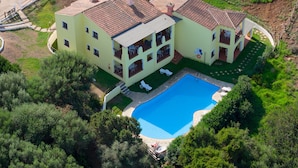 A two-story building with a swimming pool, surrounded by greenery and a fenced area. - Graziose Ville con A.C e piscina comune (Stintino)