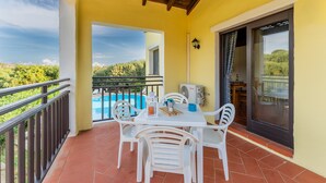 A balcony with white plastic chairs and a table, overlooking a swimming pool and greenery. - Graziose Ville con A.C e piscina comune (Stintino)