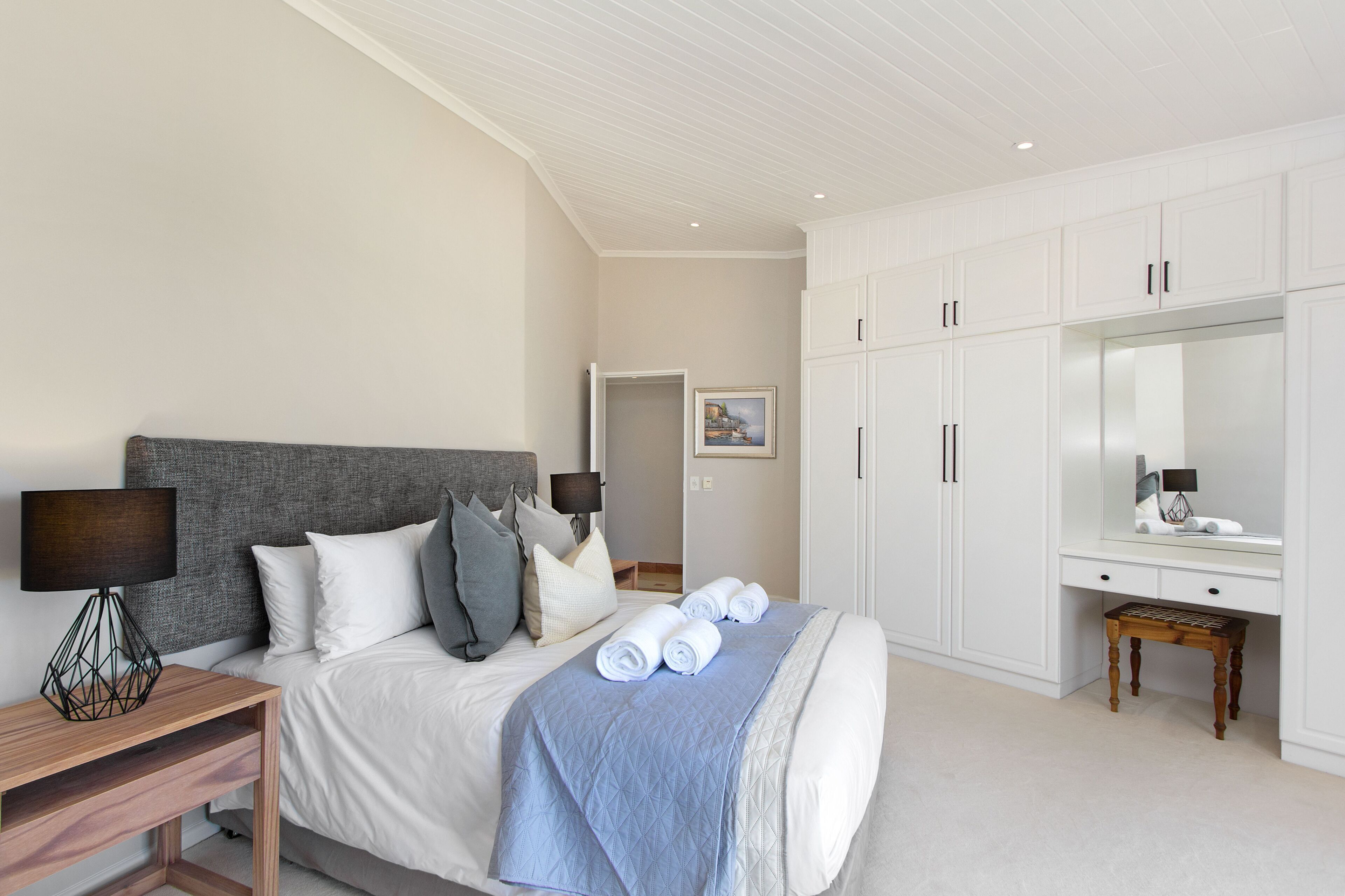 A neatly arranged bedroom with a bed, bedside tables, a desk, and a large mirror.
