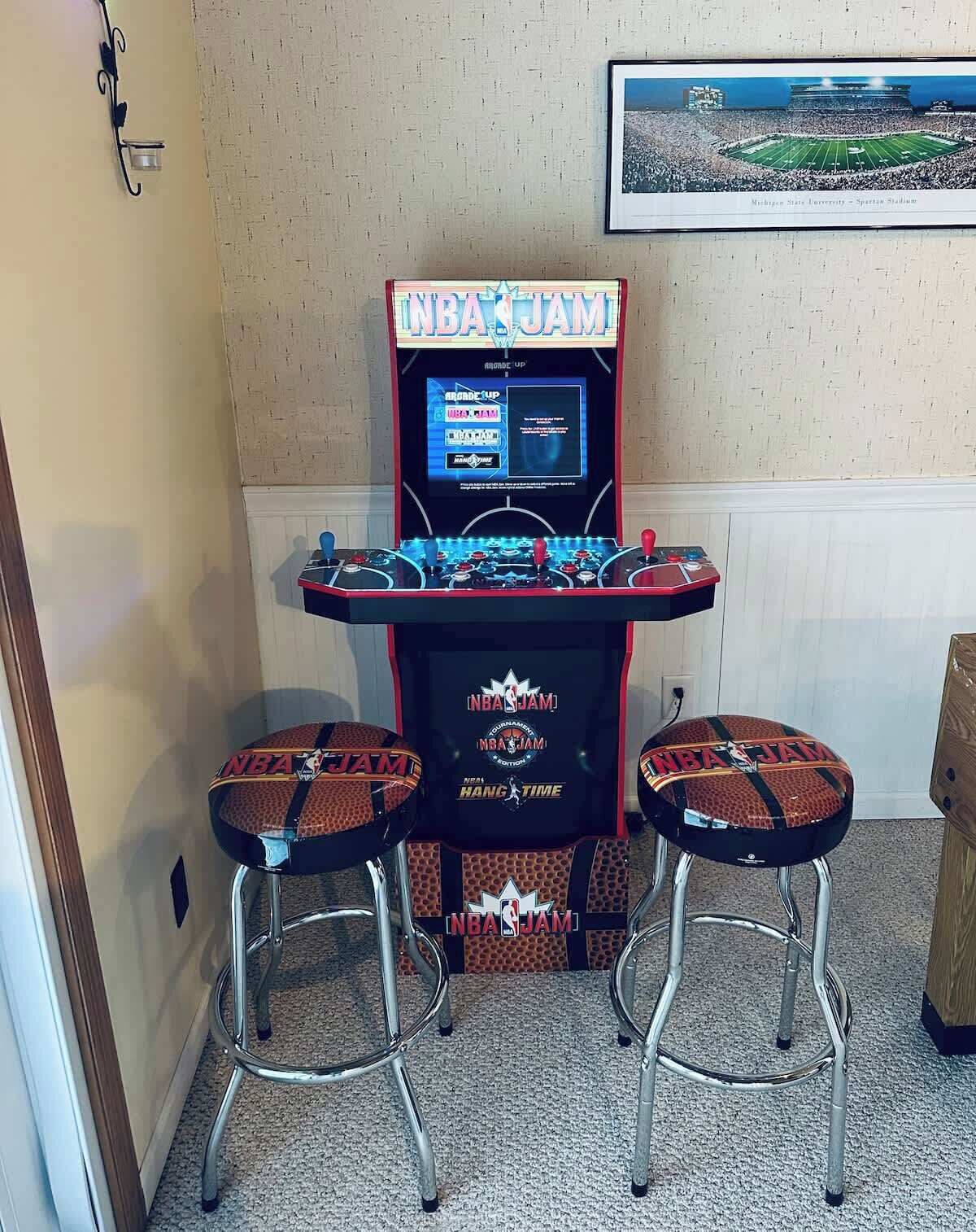 A retro arcade machine with two stools, featuring NBA JAM branding.