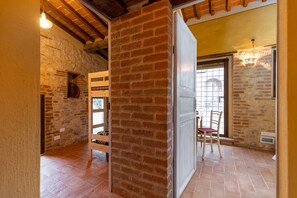 A room with exposed brick walls, a wooden ceiling, a bed, a chair, and a window with a view.