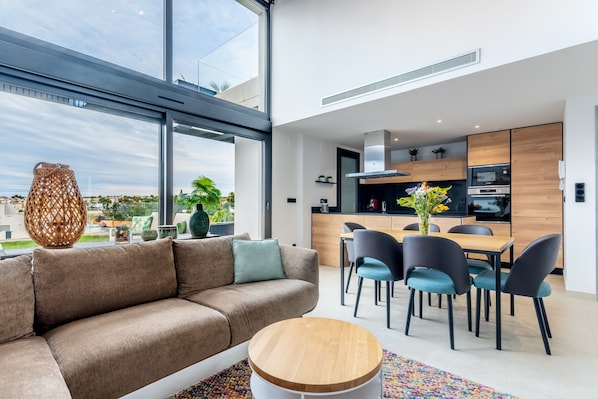 A modern living room with a sofa, dining table, chairs, and a large window.