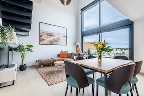 A modern living room with a dining area, large windows, and a view of the city.