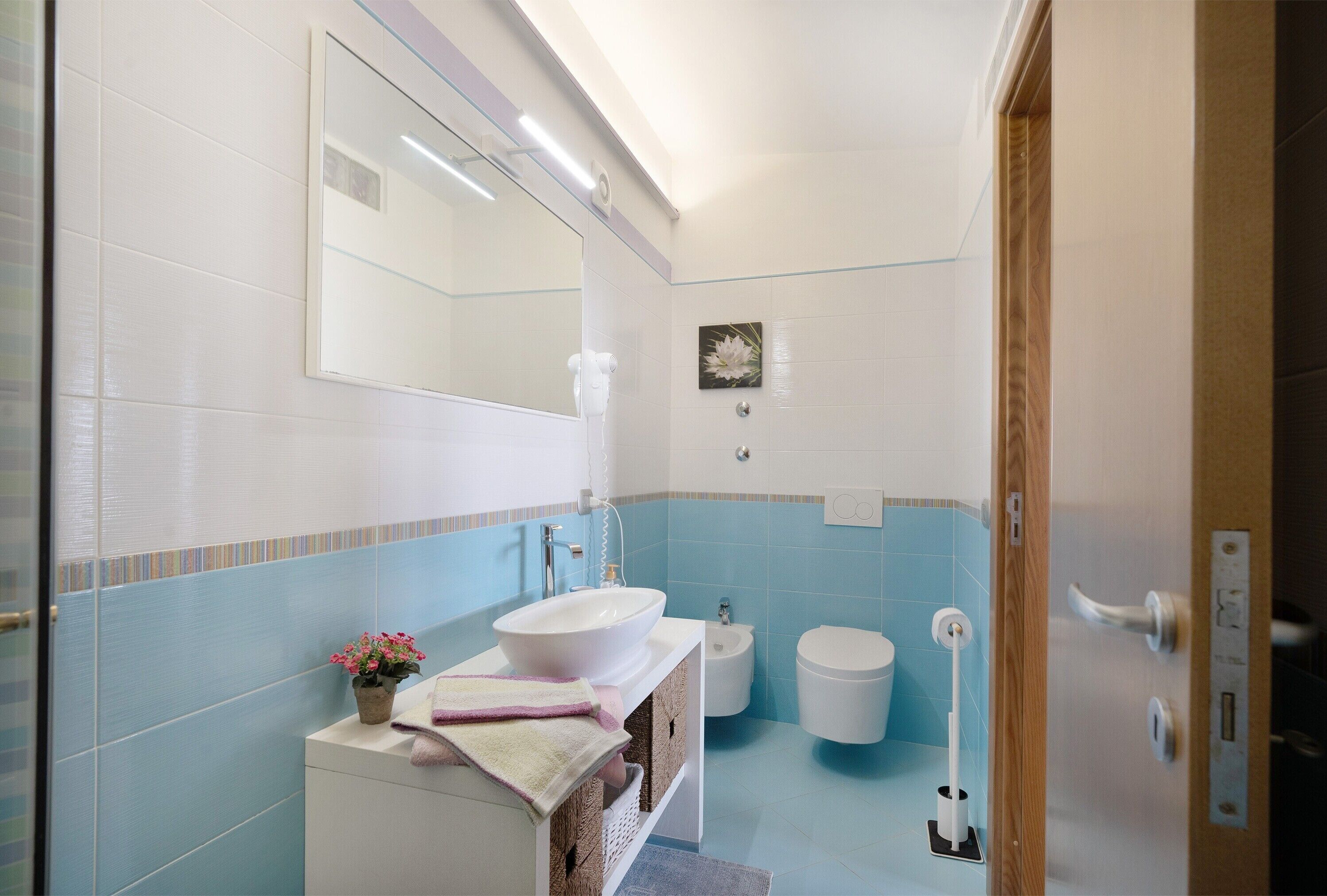 Een badkamer met een witte wastafel, een spiegel, een bidet en een toilet.