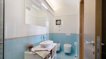 Een badkamer met een witte wastafel, een spiegel, een bidet en een toilet.