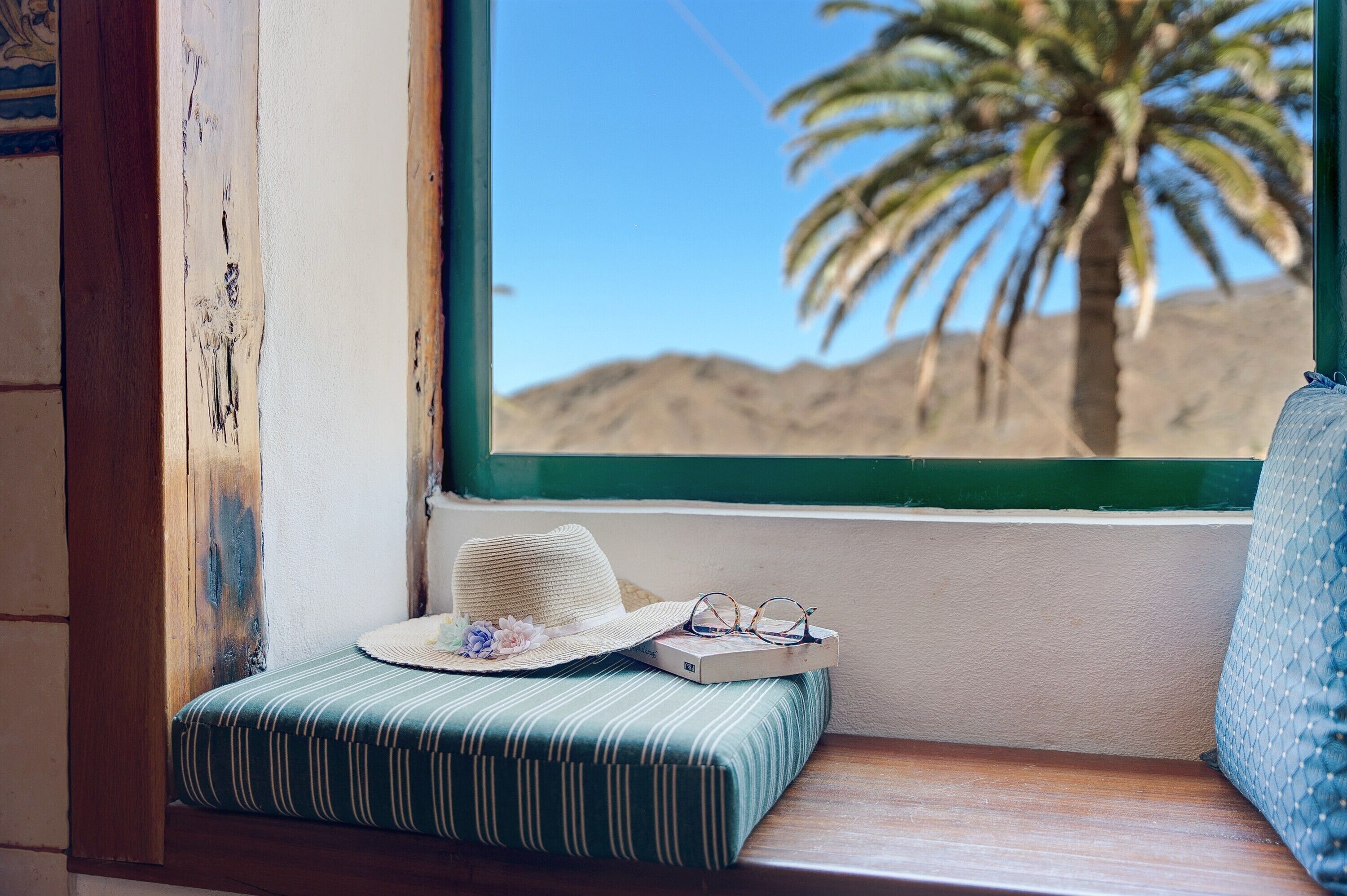 Un siège de fenêtre avec un coussin à rayures, un chapeau et une paire de lunettes posées sur un livre.