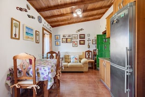 A kitchen with a refrigerator, wooden cabinets, a dining table with chairs, and a sofa.