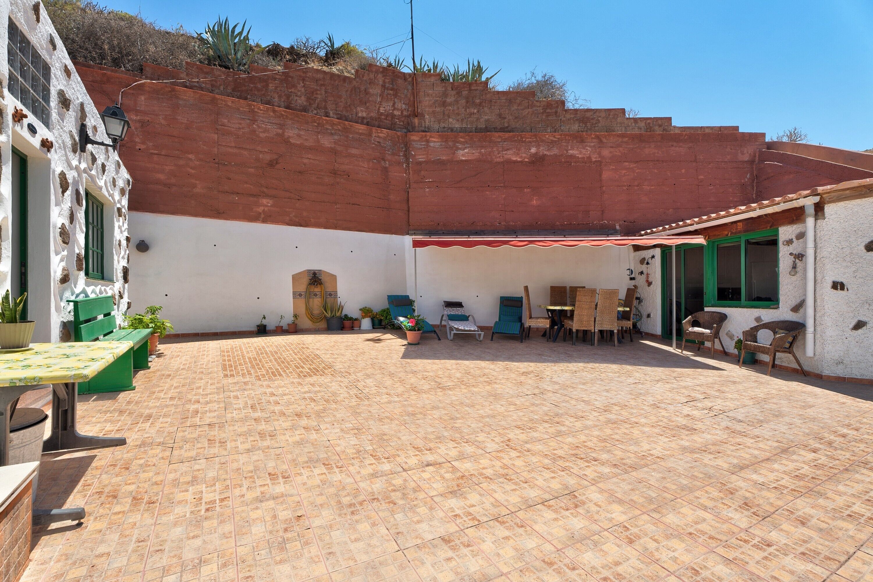 A courtyard with a tiled floor, a table with chairs, and a small building with a red awning.