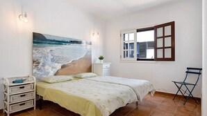 Une chambre avec un lit, une table de chevet, une chaise, une fenêtre avec des stores et une fresque murale représentant une plage.