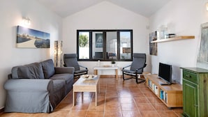Un salon comprenant un canapé, des fauteuils, une table basse, un téléviseur et une bibliothèque.