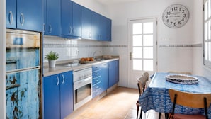 Une cuisine avec des meubles de rangement bleus, un four blanc, un évier et une table à manger avec des chaises.